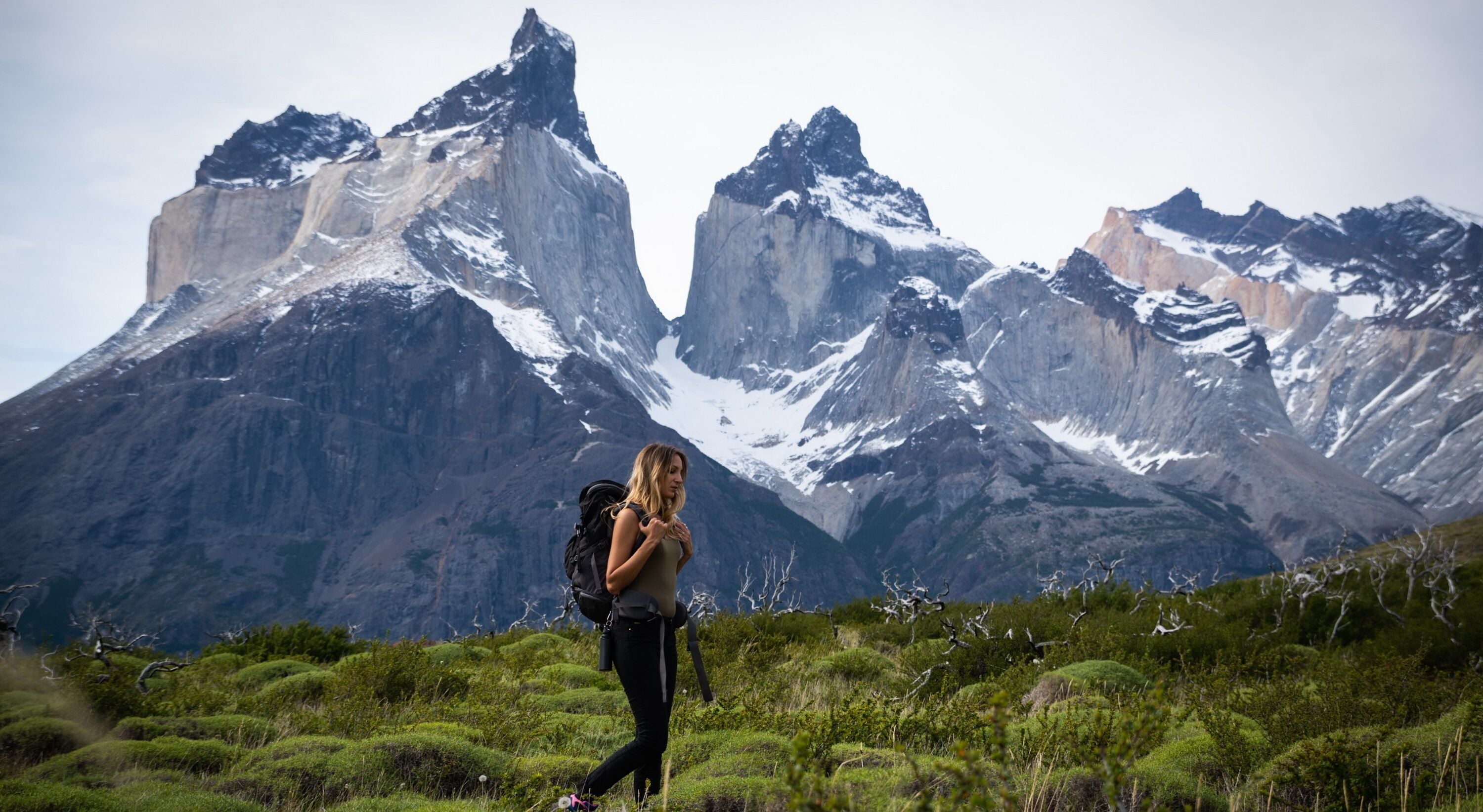 A person hiking with a backpack in a mountainous area with snow-capped peaks in the background.