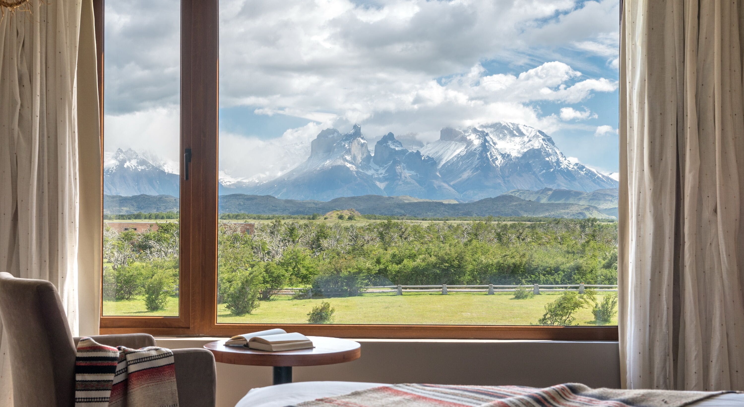 Habitación de hotel con un ventanal que ofrece vistas a montañas nevadas y un paisaje verde.