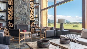 A cozy living room with a stone fireplace, wooden furniture, and a view of the mountains. - Rio Serrano Hotel + Spa (Torres del Paine)