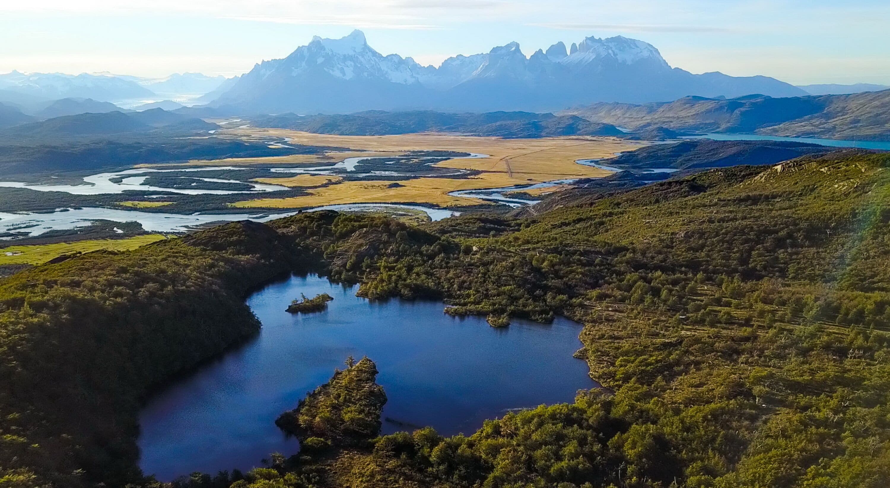 Paisagem montanhosa com um lago rodeado por vegetação e um rio.