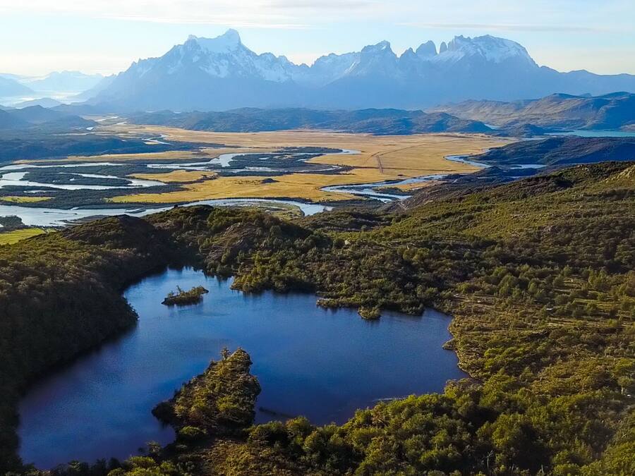 Paisagem montanhosa com um lago rodeado por vegetação e um rio.