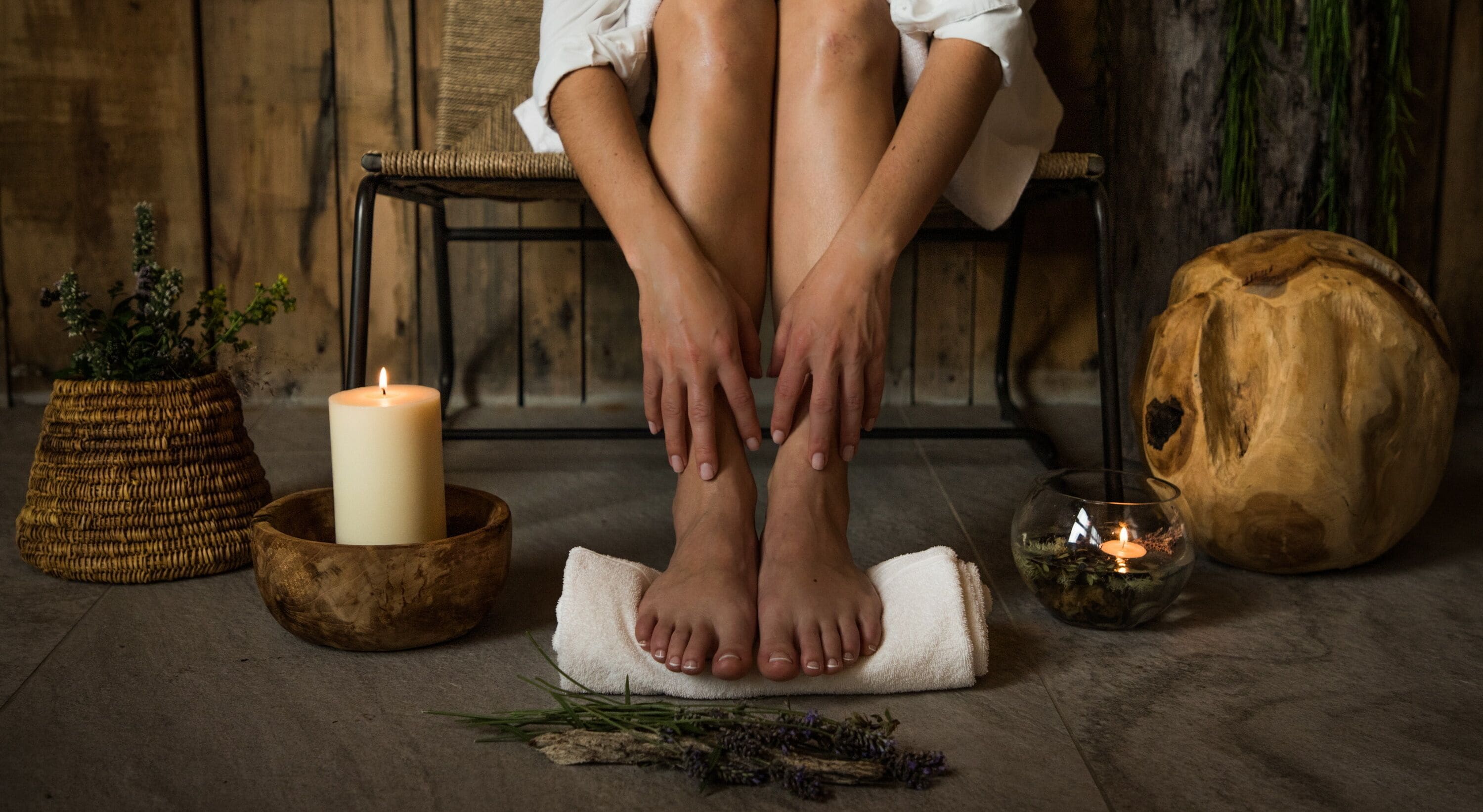 Uma pessoa sentada com as pernas cruzadas, os pés sobre uma toalha, rodeada por velas, uma tigela de madeira e uma abóbora decorativa.