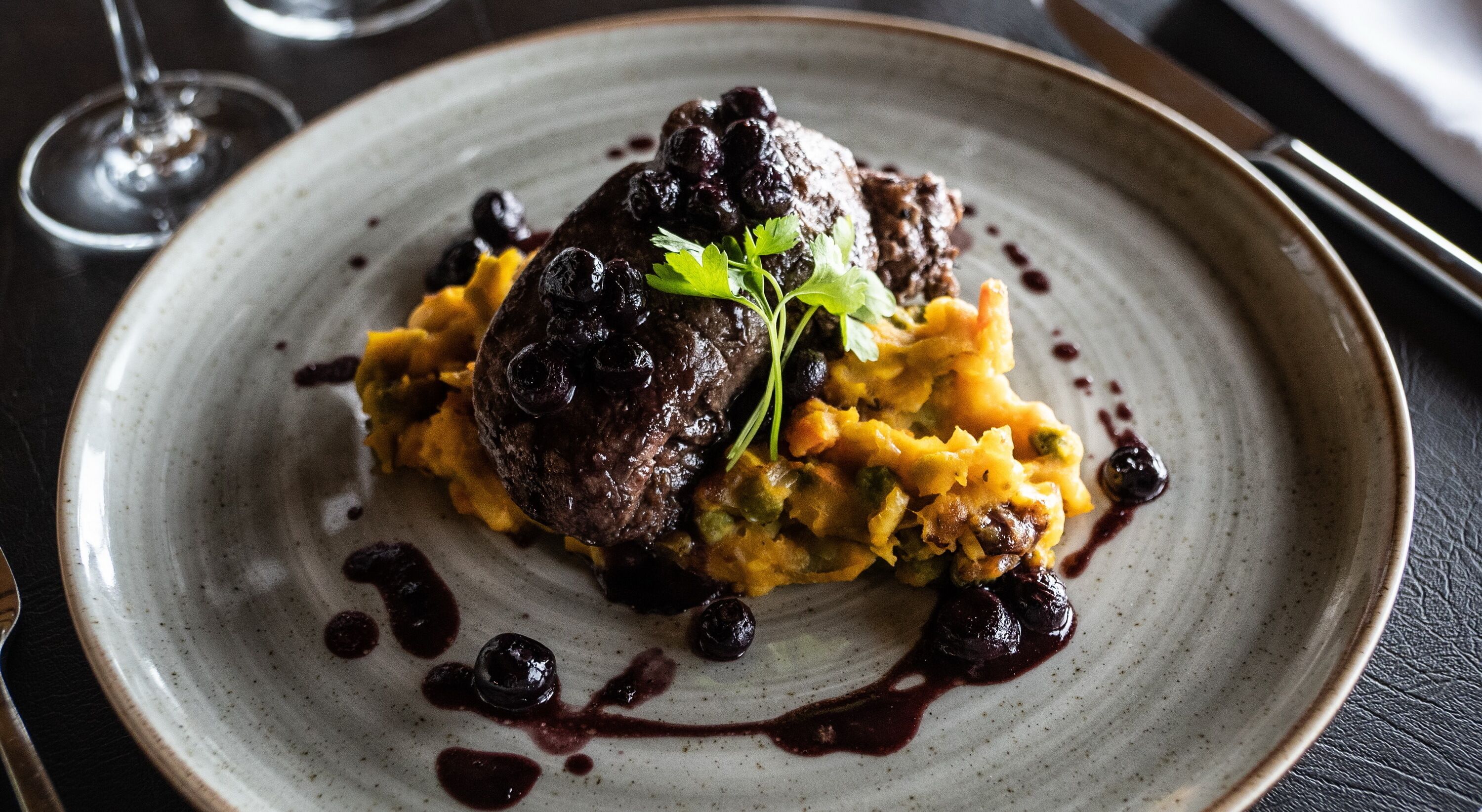 Een bord met een vleesgerecht, puree en een bessensaus.