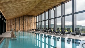 Una piscina interior con paredes de madera y ventanas amplias que ofrecen vistas a las colinas.