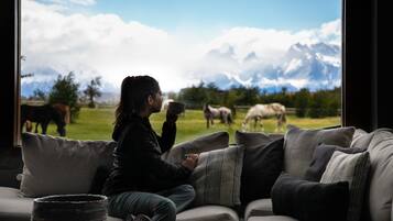 A person sitting on a couch with a view of horses grazing in a field and mountains in the background.