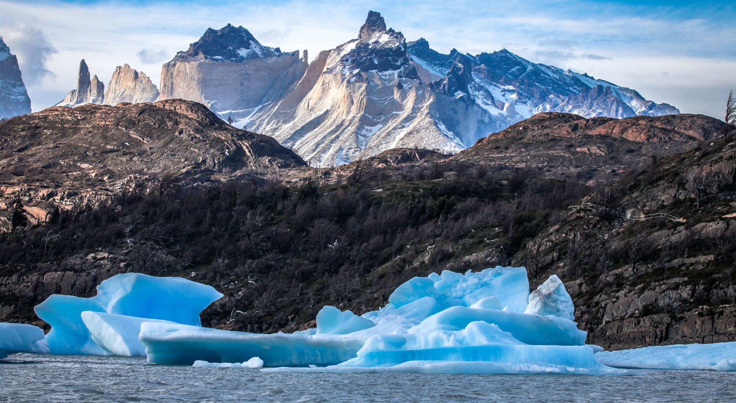 A mountainous landscape with prominent peaks and icebergs in the foreground.