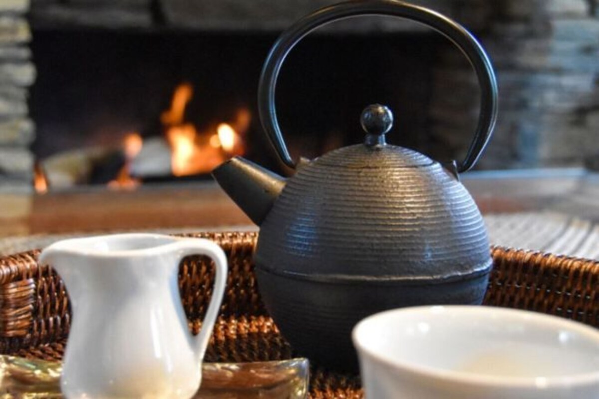 A teapot, a white pitcher, and a cup on a woven mat with a fireplace in the background.