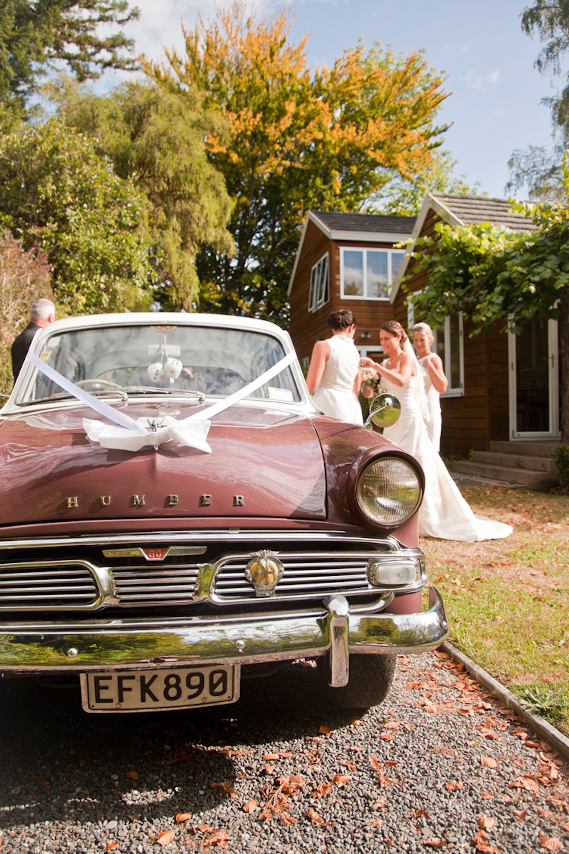 A vintage car with a visible license plate and a wedding party in the background.