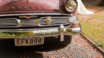 A vintage car with a visible license plate and a wedding party in the background.