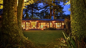 A modern house with large glass windows, surrounded by trees and a well-maintained lawn. - River Birches (Turangi)