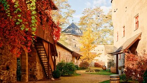 Un sentier pavé de pierres mène à travers un village pittoresque, avec des bâtiments en pierre, un escalier en bois et un tonneau au premier plan.