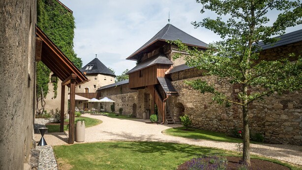 Une cour bordée de murs en pierre, avec des bâtiments en bois et un arbre.