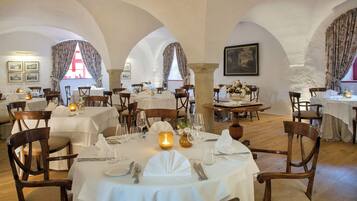 A restaurant with multiple tables set for dining, featuring white tablecloths, wooden chairs, and candlelit centerpieces.