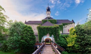 A historic building with a clock tower, an arched entrance, and a wooden bridge leading to it.