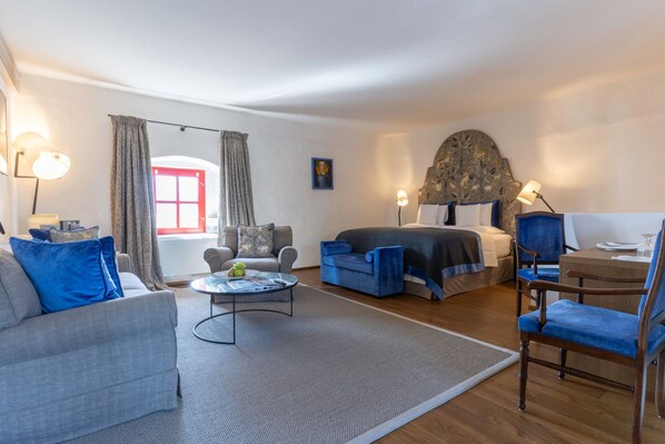 A modern hotel room with a large bed, a sofa, a chair, a small table, and a desk.