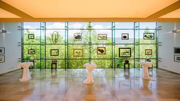 A spacious gallery with a large window, framed artwork, and three tables with white tablecloths.