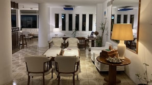 A spacious living area with a dining set, a sofa, and a coffee table. There is a large mirror on the wall and a lamp on a side table. - Hotel Alhambra (Punta del Este)