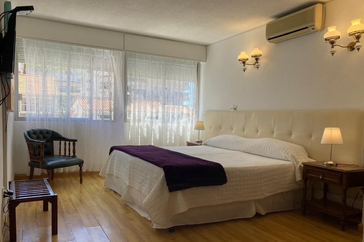 Un dormitorio con cama, una silla, una mesita de noche y una lámpara.