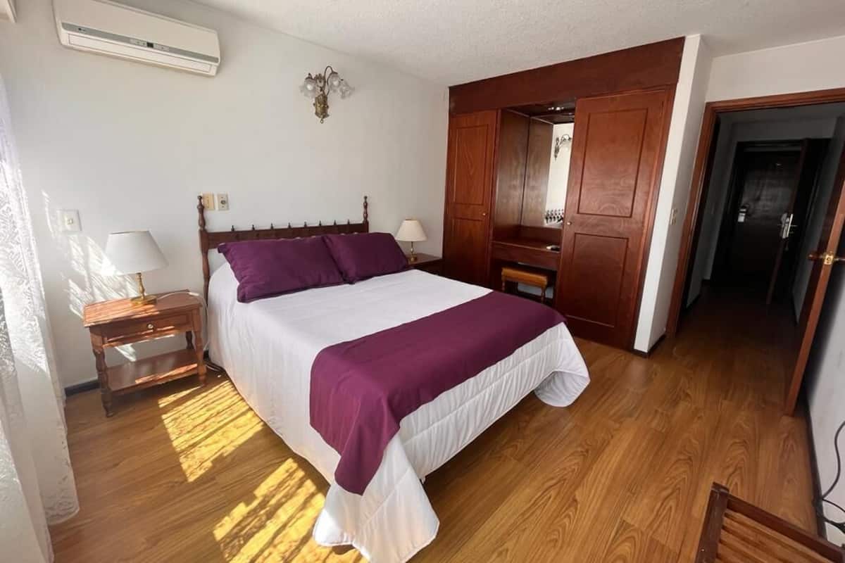 Un dormitorio con cama, armario de madera y mesita de noche con lámpara.