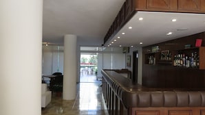 A bar area with a high counter and shelves of bottles. There is a seating area with tables and chairs in the background. - Hotel Alhambra (Punta del Este)