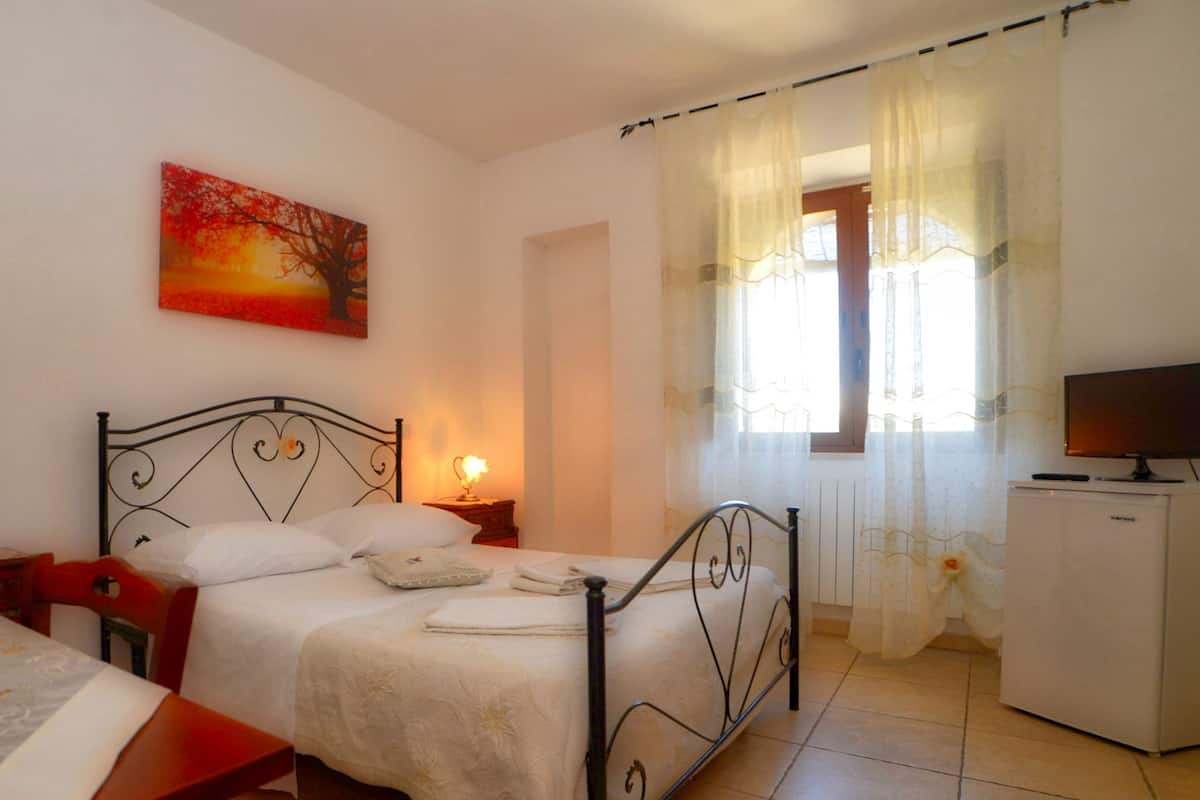 Ein Schlafzimmer mit Bett, Fernseher, kleinem Kühlschrank, Blumenvase und einem Bild an der Wand.