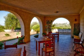 An outdoor patio with a table and chairs, surrounded by arches, and a view of greenery outside.