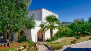 A white building with an arched entrance, surrounded by lush greenery and a paved pathway.