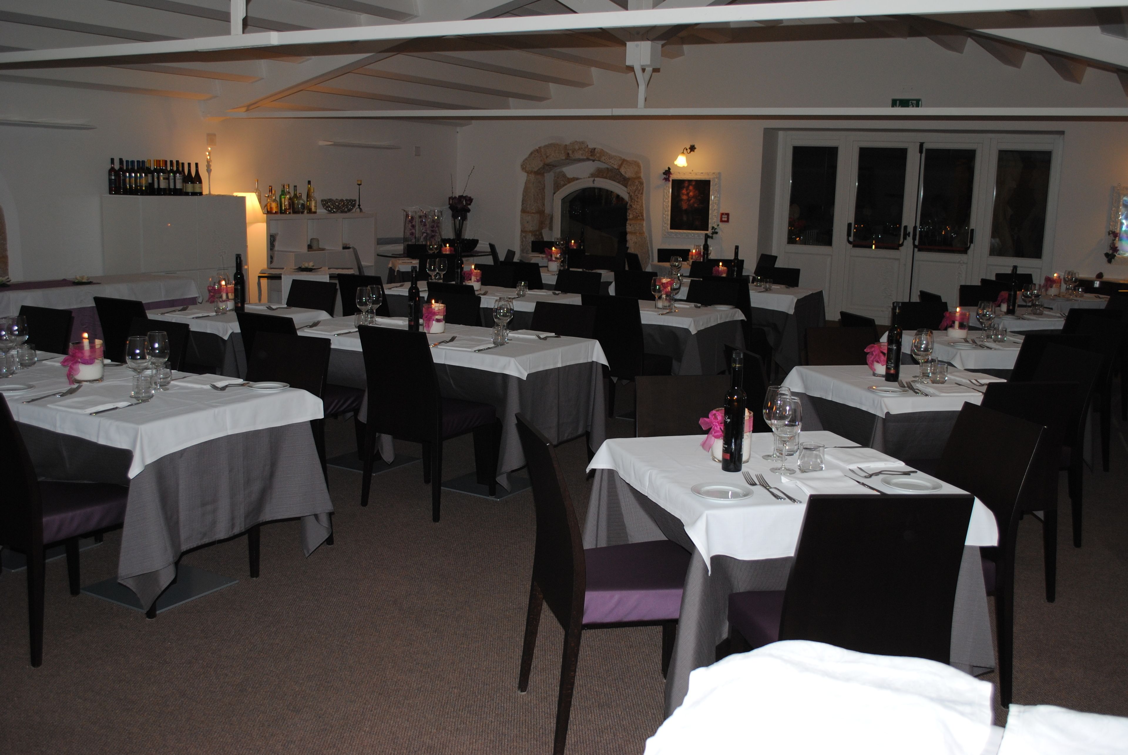 A restaurant with multiple tables set for dining, featuring white tablecloths and black chairs.
