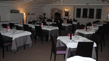 A restaurant with multiple tables set for dining, featuring white tablecloths and black chairs.