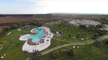 An aerial view of a resort with a large, winding pool surrounded by lounge areas and a well-maintained lawn.