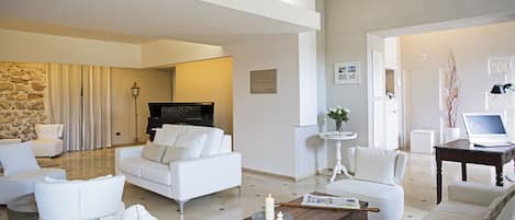 A modern living room with white furniture, a stone accent wall, and a piano.