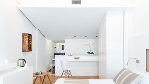 Una habitación de hotel moderna y compacta con kitchenette, un pequeño comedor y una cama con almohada a rayas.