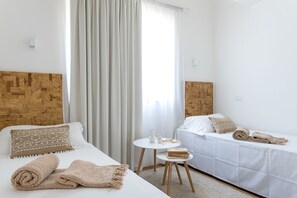 Two beds with patterned pillows and a small table with a vase and glasses.
