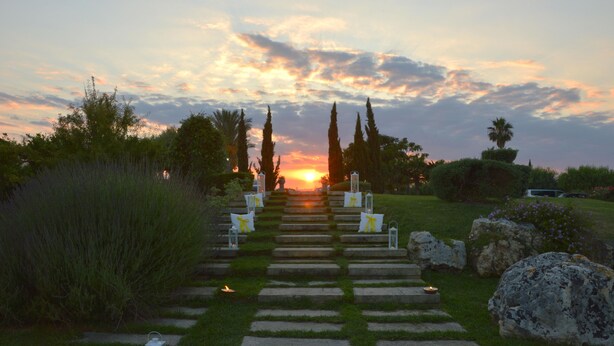 Un sendero de piedra que conduce a una vista del atardecer, bordeado por faroles y follaje.