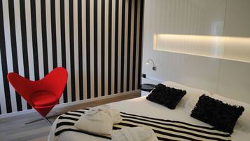 Ein modernes Hotelzimmer mit gestreifter Wand, einem roten Sessel, einem Bett mit schwarz-weißer Bettwäsche und einem Nachttisch mit Lampe.