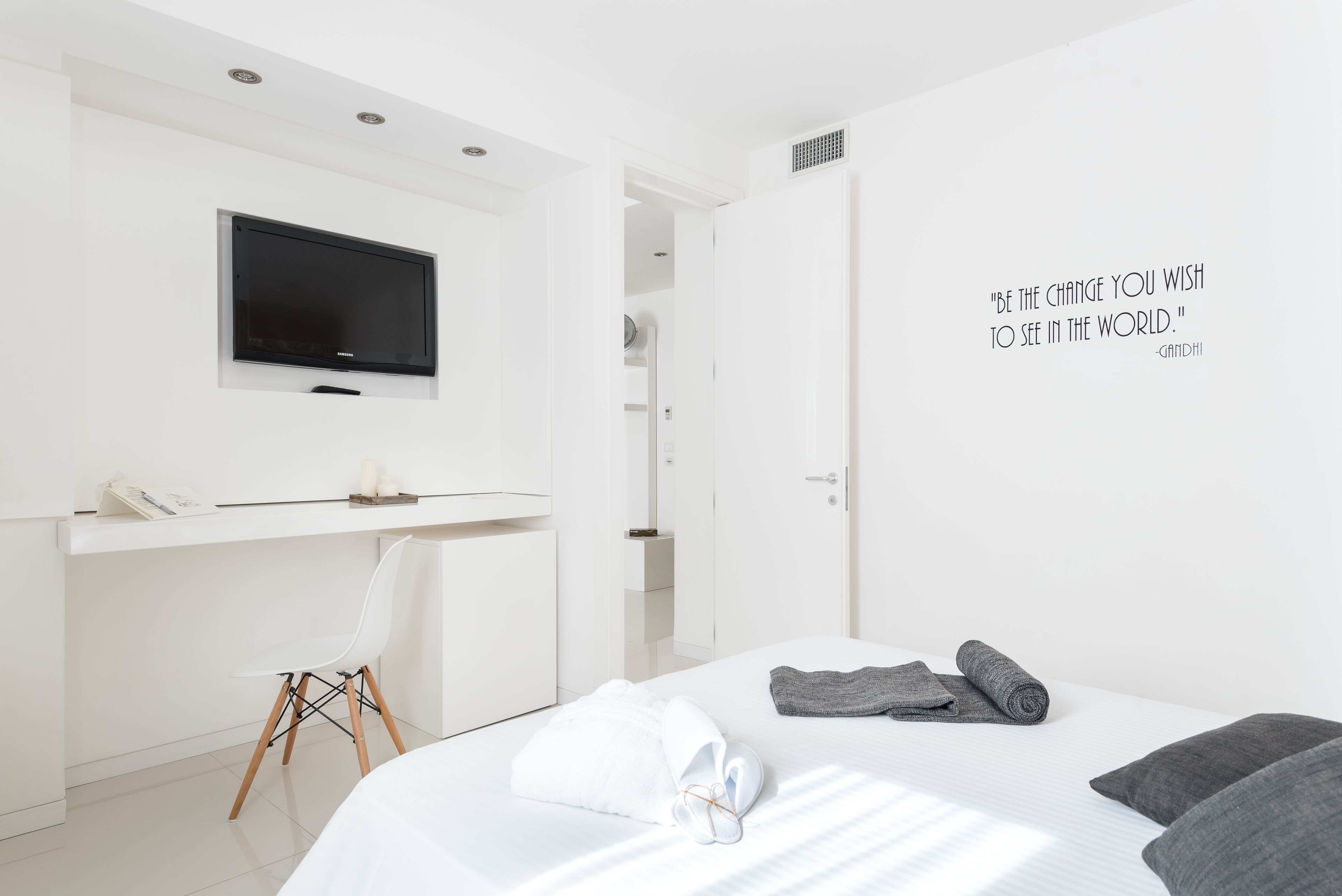 A modern hotel room with a bed, a desk, a chair, and a TV.