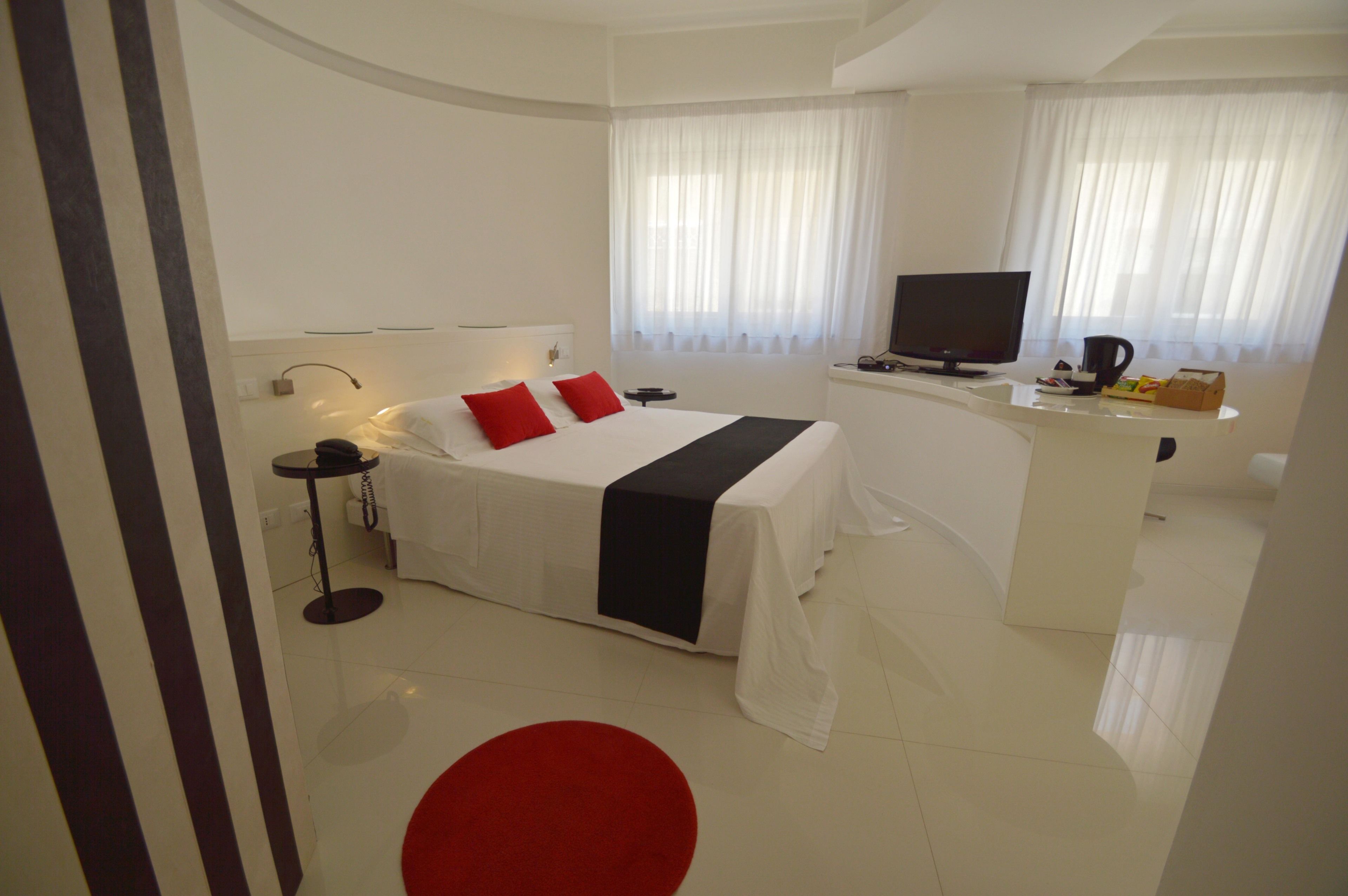 A modern hotel room with a large bed, a desk, a TV, and a red accent chair.