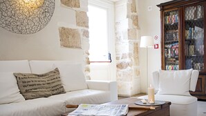 Una sala de estar acogedora con un sofá blanco, una mesa de centro de madera con periódicos y una estantería llena de libros.