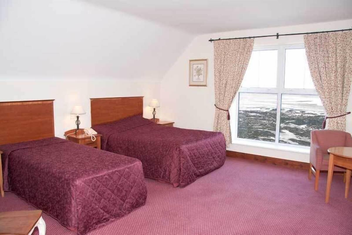 Habitación de hotel con dos camas, una mesita, una silla y ventana con vista al mar.