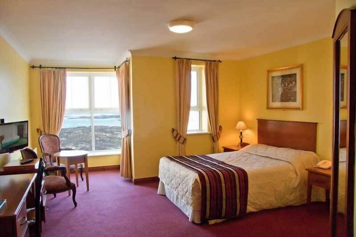 Habitación de hotel con cama, escritorio, silla y un amplio ventanal con vistas.