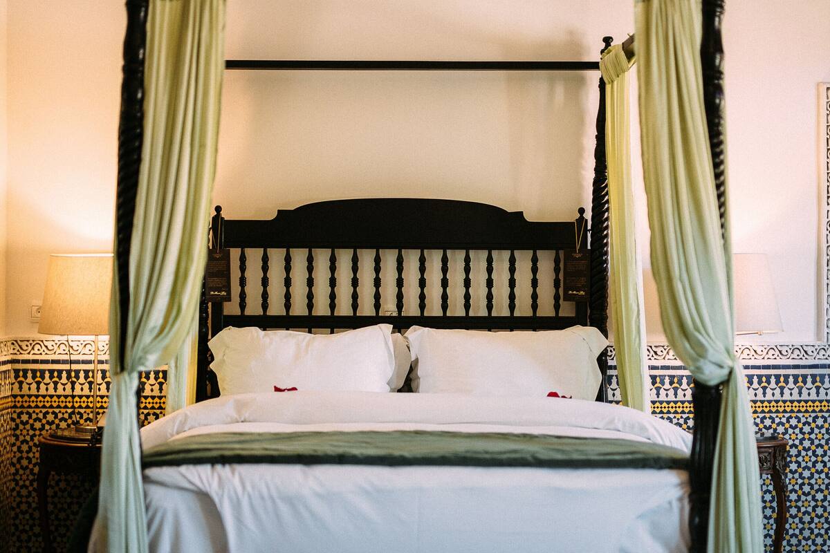 Una cama con dosel y cortinas, suelo estampado y pared con decoración ornamental.