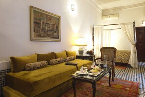 A room with a yellow sofa, a table with a tray of food, a chair, a lamp, and a painting on the wall. - La Maison Bleue Batha (Fes)