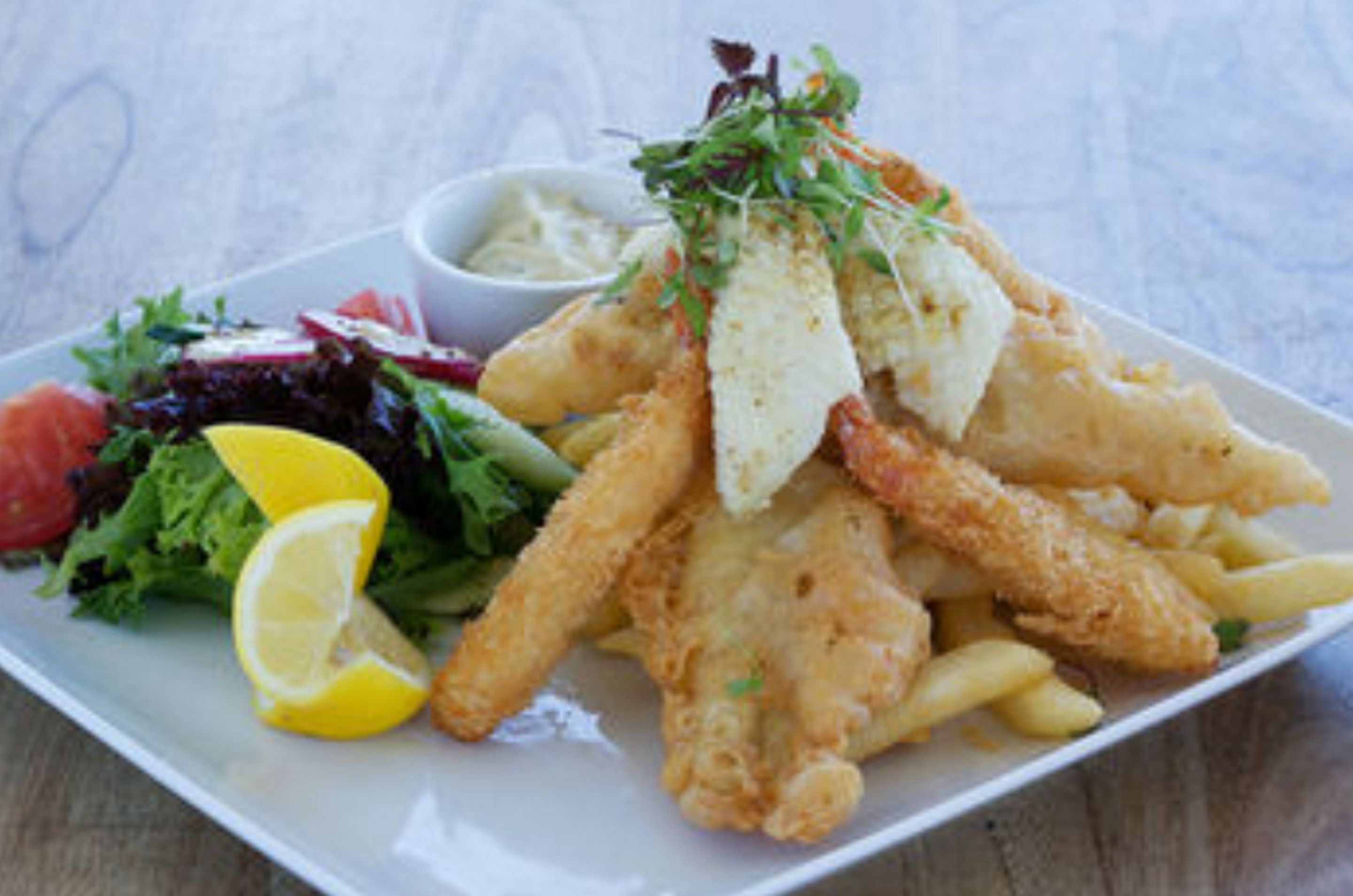 A plate of fish and chips with a side salad and lemon wedge.