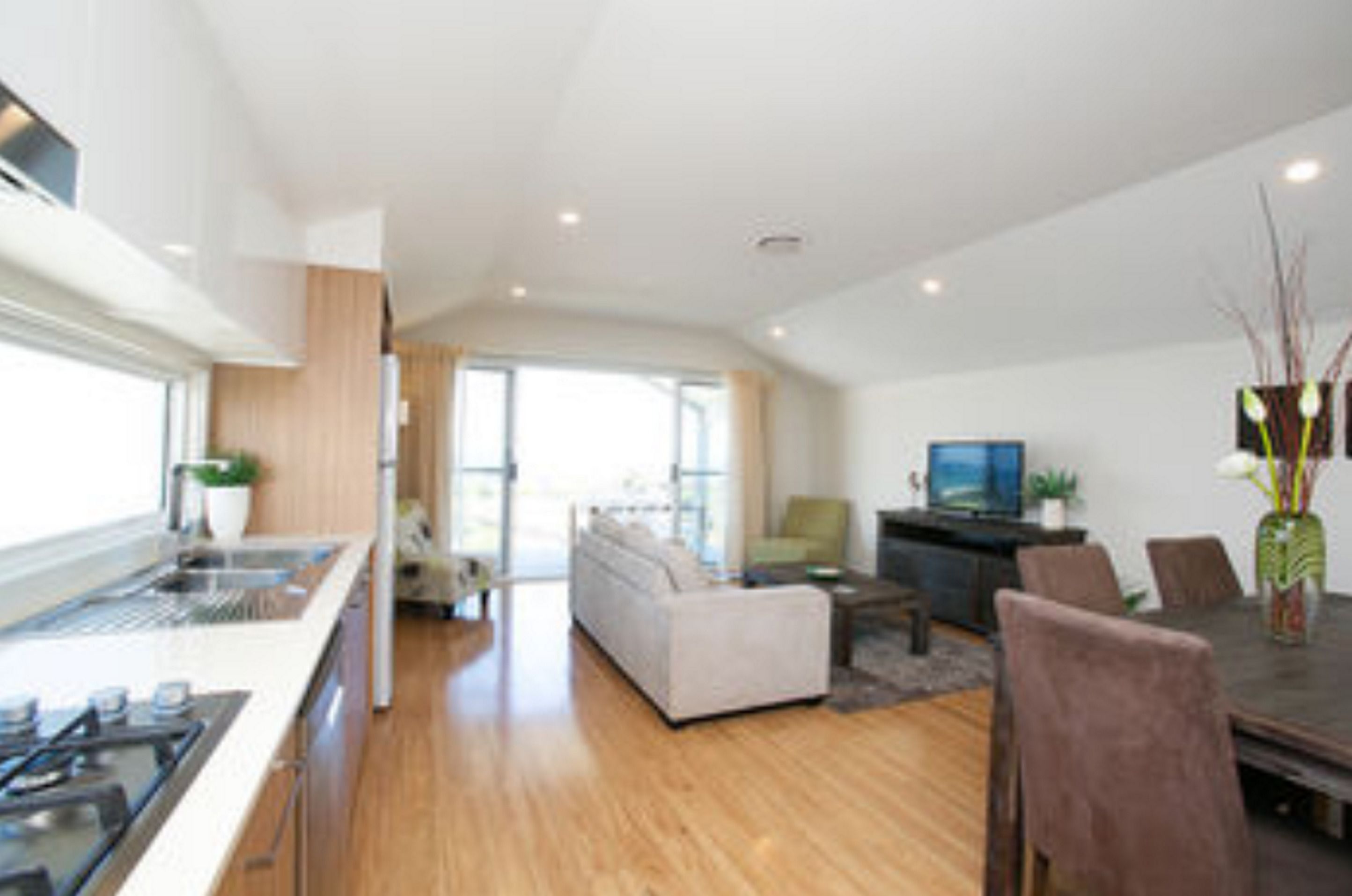 A modern kitchen with a central island, a dining area with a table and chairs, and a living room with a sofa and a TV.