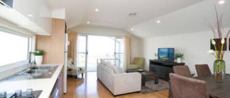 A modern kitchen with a central island, a dining area with a table and chairs, and a living room with a sofa and a TV.