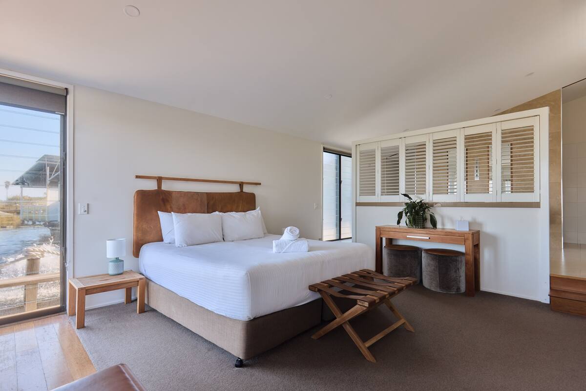 Une chambre d’hôtel moderne avec un grand lit, un banc en bois, une petite table et une vue sur l’extérieur.