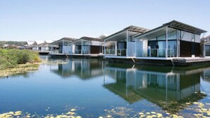 Une rangée de maisons modernes à façade vitrée, situées au bord d’une étendue d’eau paisible.
