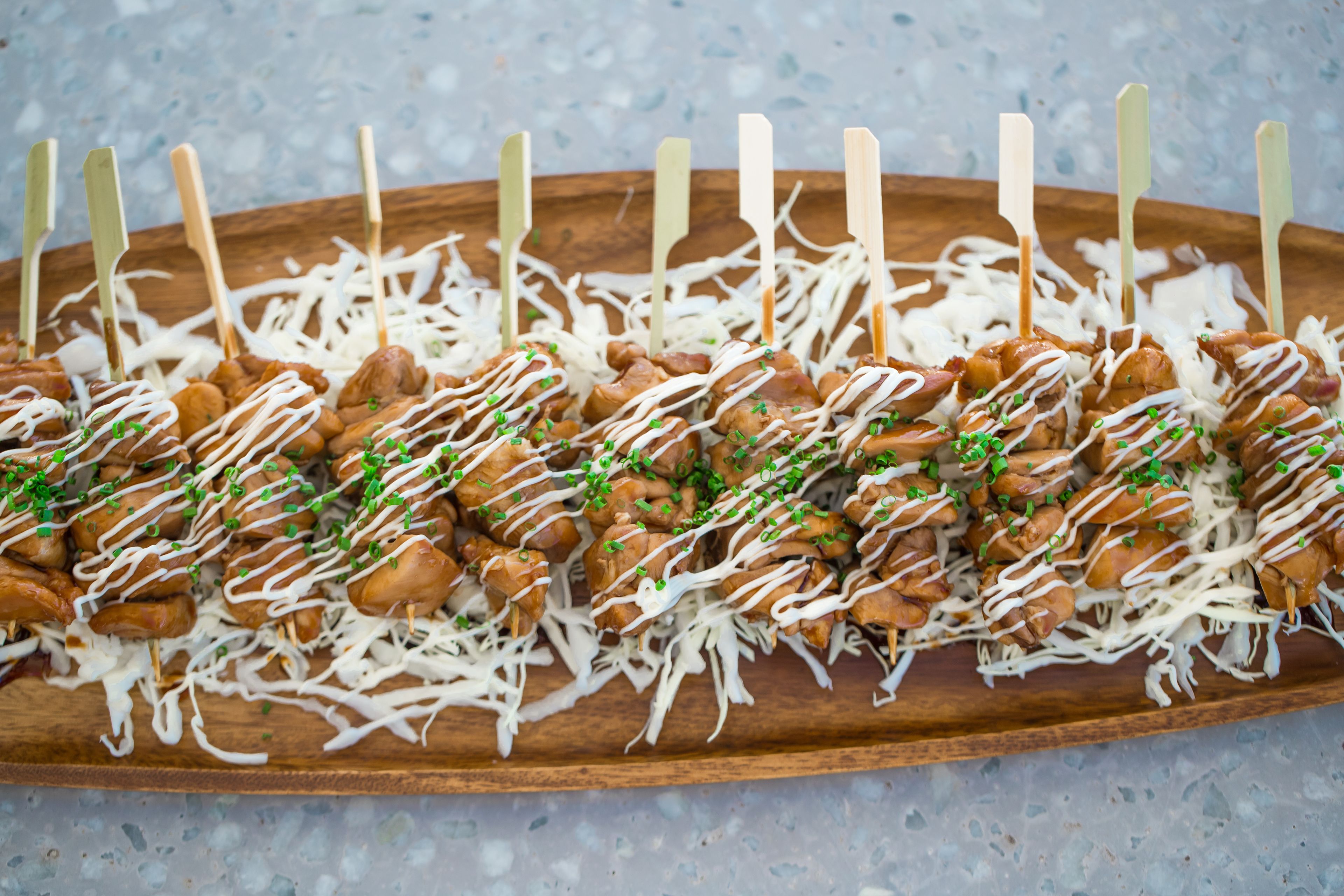 A wooden tray with skewered food items, drizzled with white sauce and garnished with green herbs.