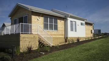 A single-story wooden house with a front porch, a small staircase, and a fenced yard.
