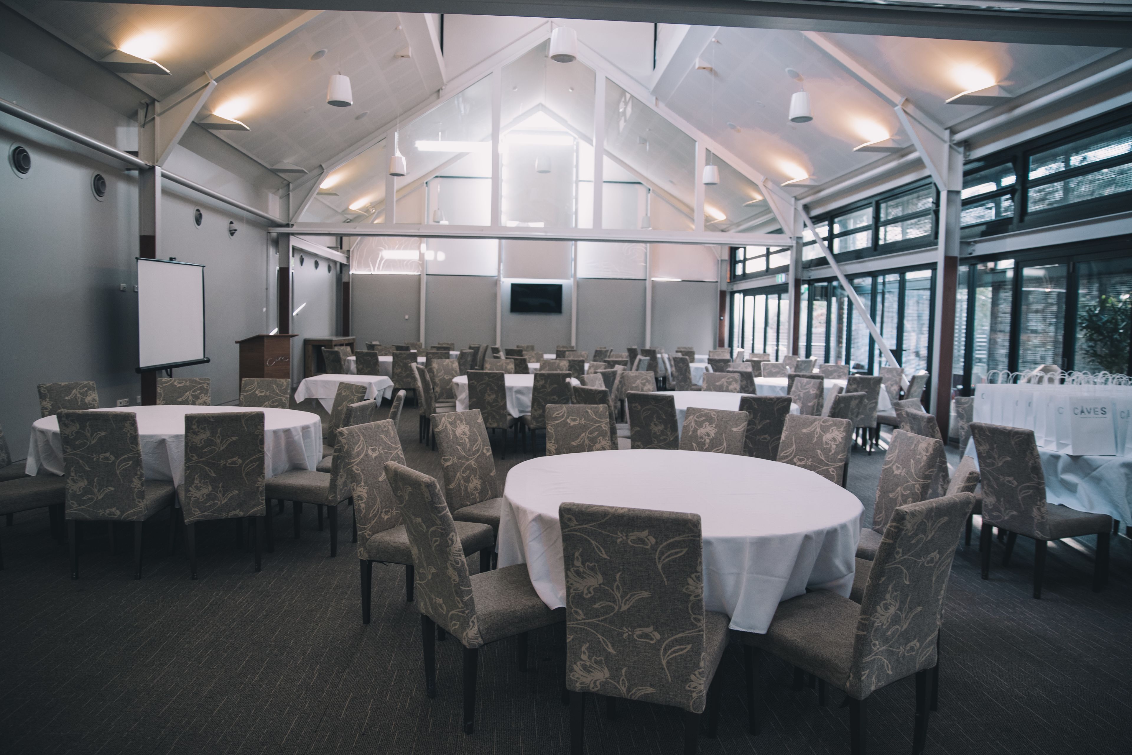 A conference room with multiple round tables, chairs, a whiteboard, and a large window providing natural light.